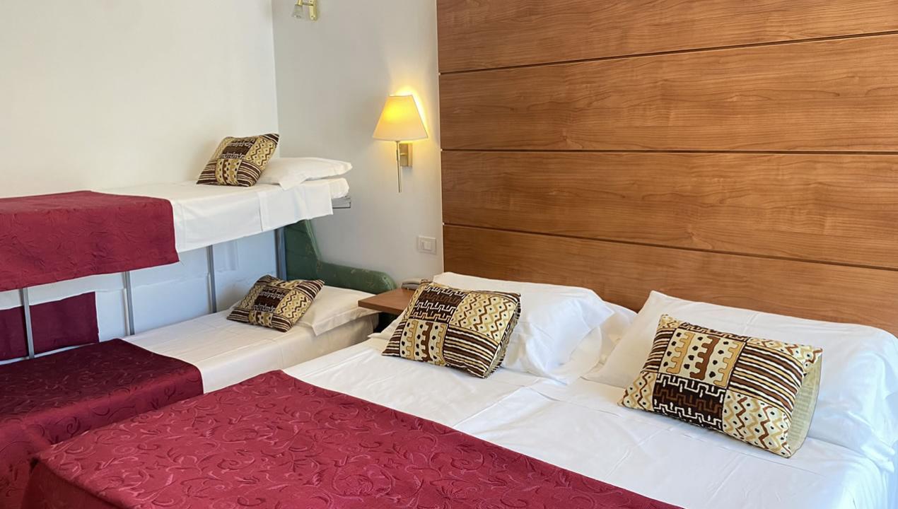 Camera d'albergo con letti a castello e matrimoniale, decorata con cuscini e copriletti rossi.