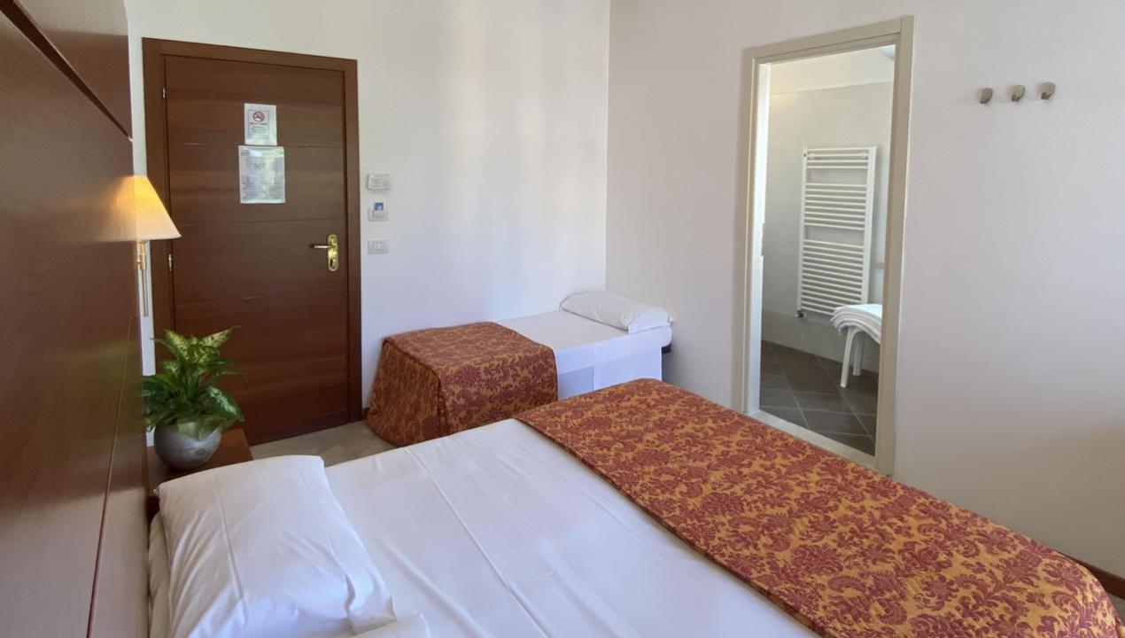 Camera d'albergo con due letti, bagno e pianta decorativa.