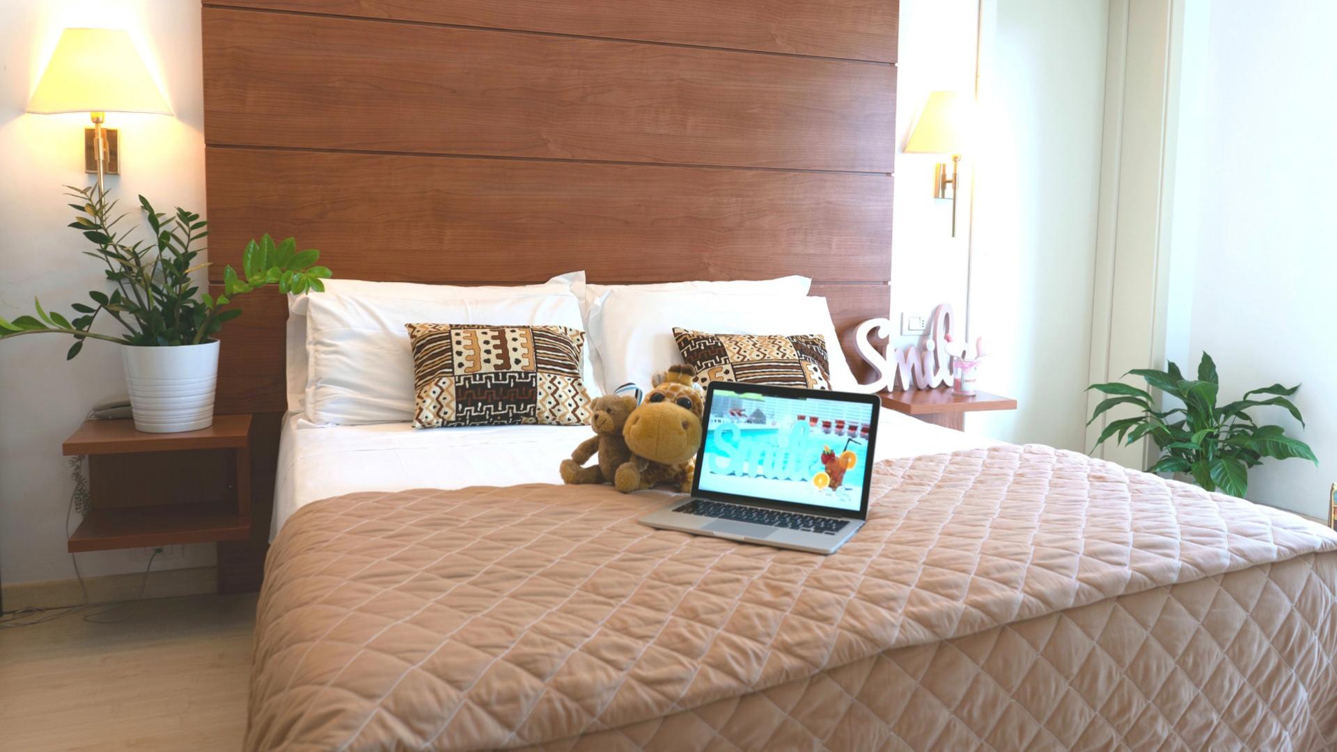 Camera da letto accogliente con laptop, piante e cuscini decorativi su letto matrimoniale.