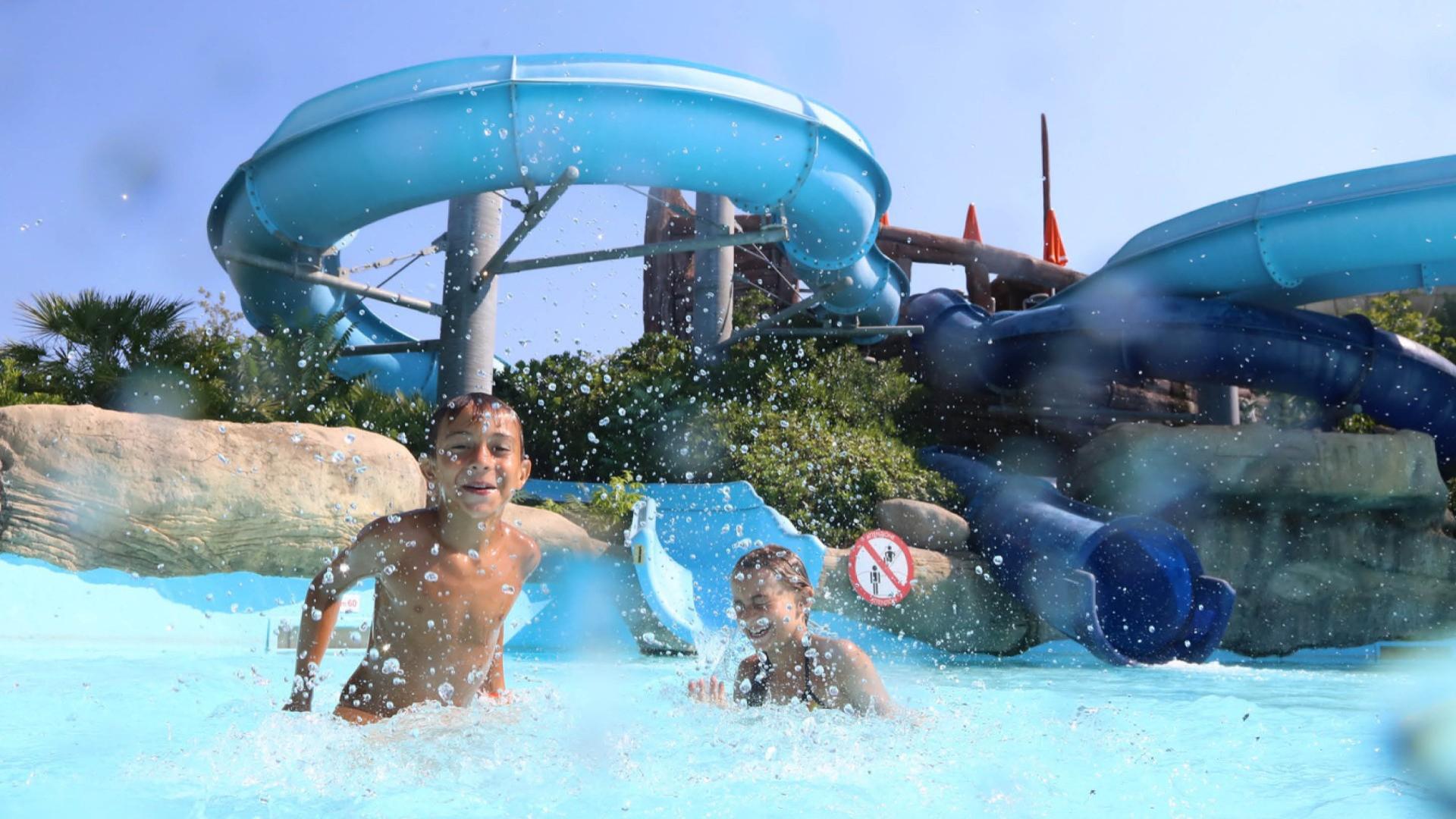 Bambini giocano felici in piscina con scivolo acquatico blu sullo sfondo.