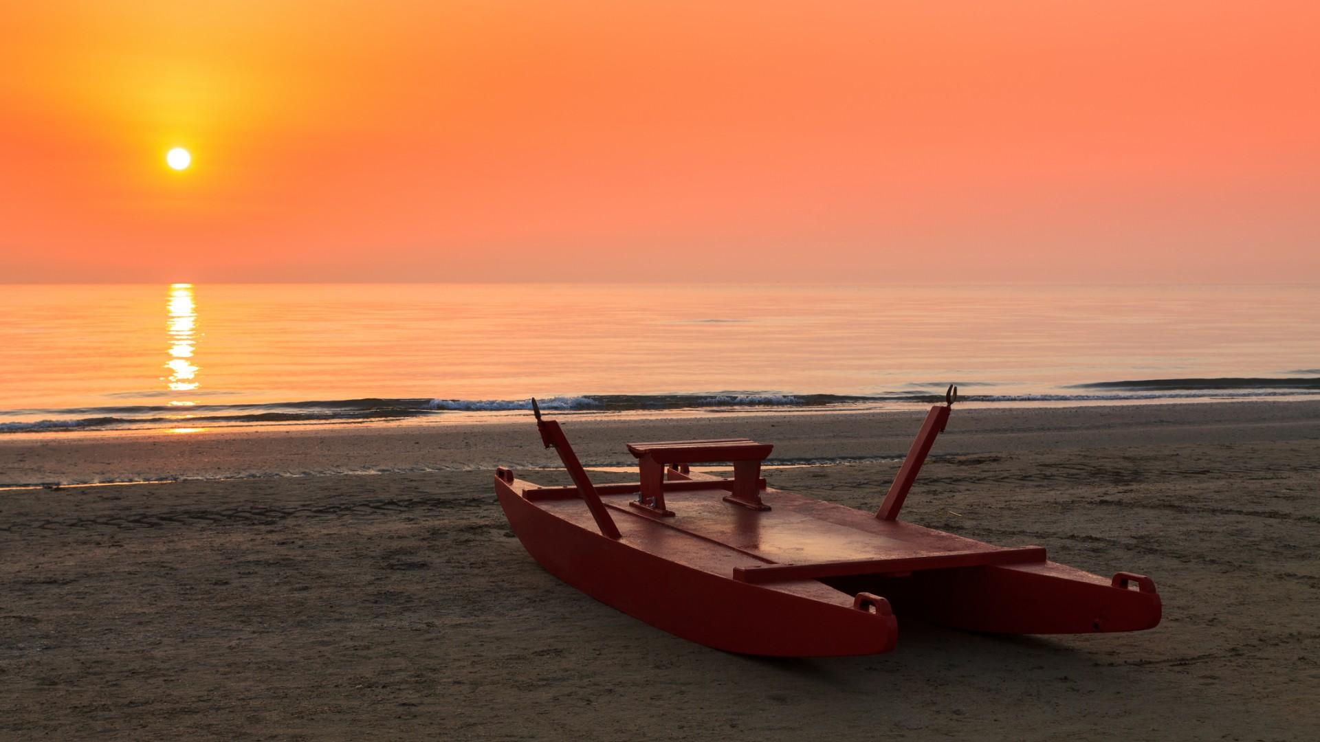 Tramonto sulla spiaggia con un pattino rosso sulla sabbia.