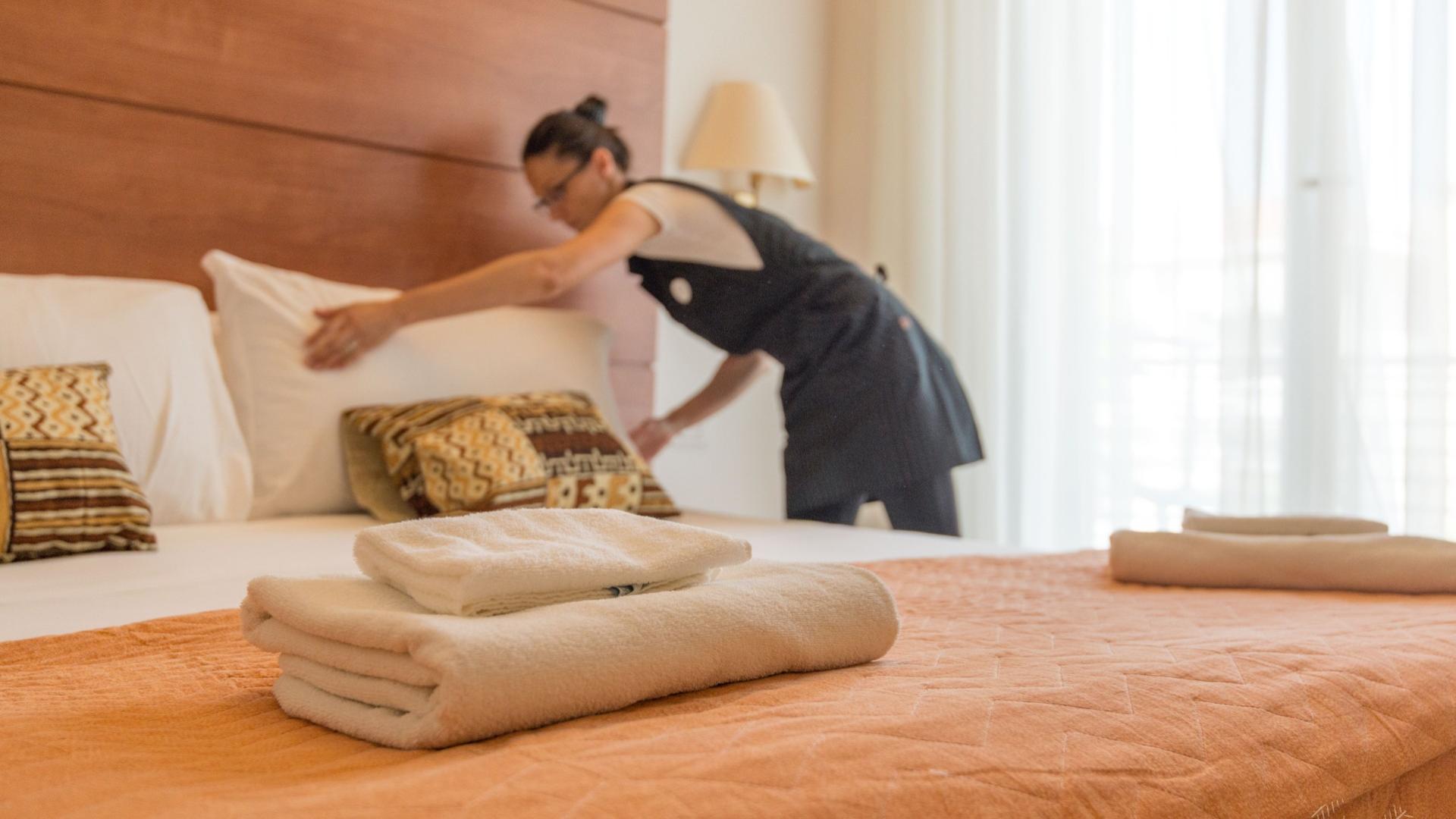 Cameriera sistema il letto in una stanza d'albergo con asciugamani piegati.