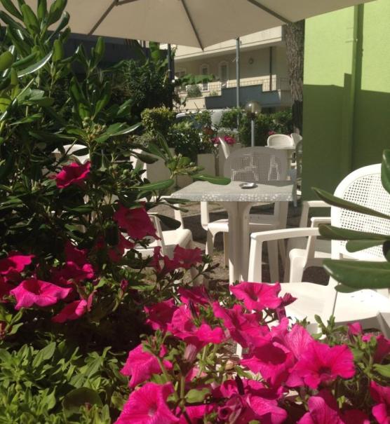 Giardino con fiori rosa, sedie bianche e ombrellone.
