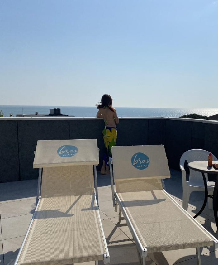 Terrazza con lettini, vista mare e persona che guarda l'orizzonte.