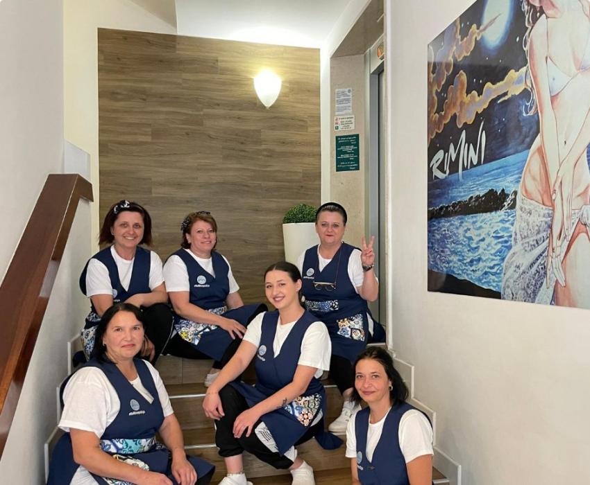 Gruppo di donne in uniforme blu, sedute su scale vicino a un poster di Rimini.